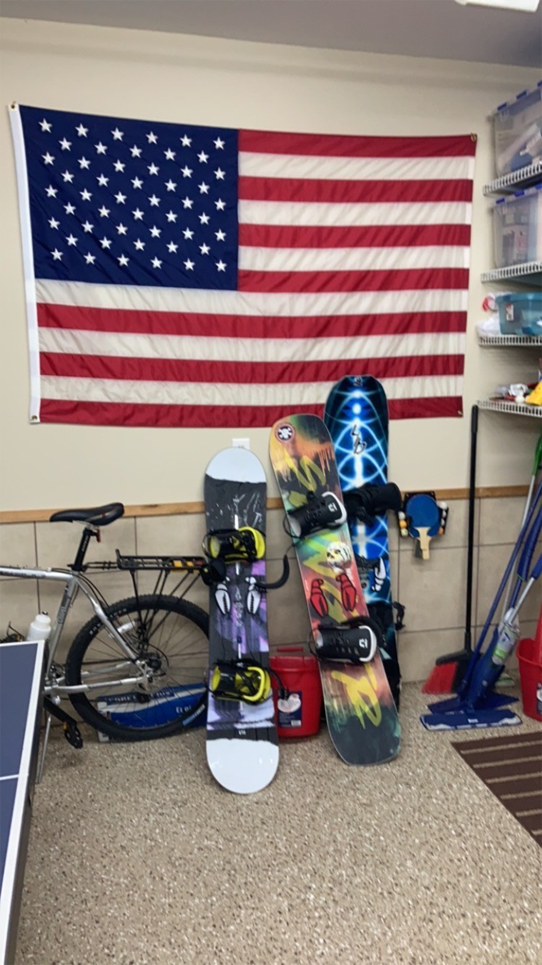 An American flag hangs on the wall above three colorful snowboards leaning against it, and a bicycle is positioned to the left.